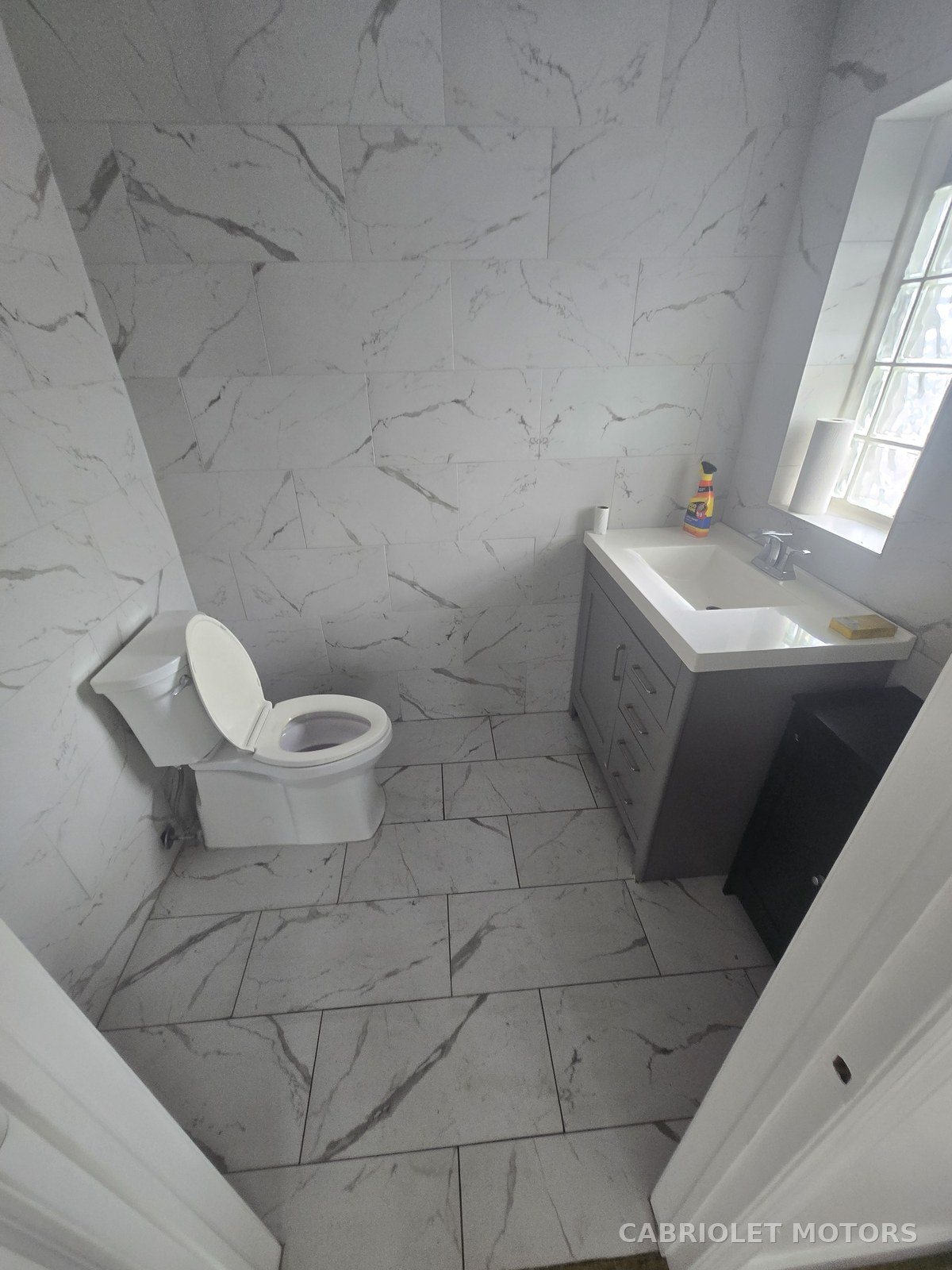 Customer bathroom before renovation, finished in white marble-look tile with a vanity, sink and window
