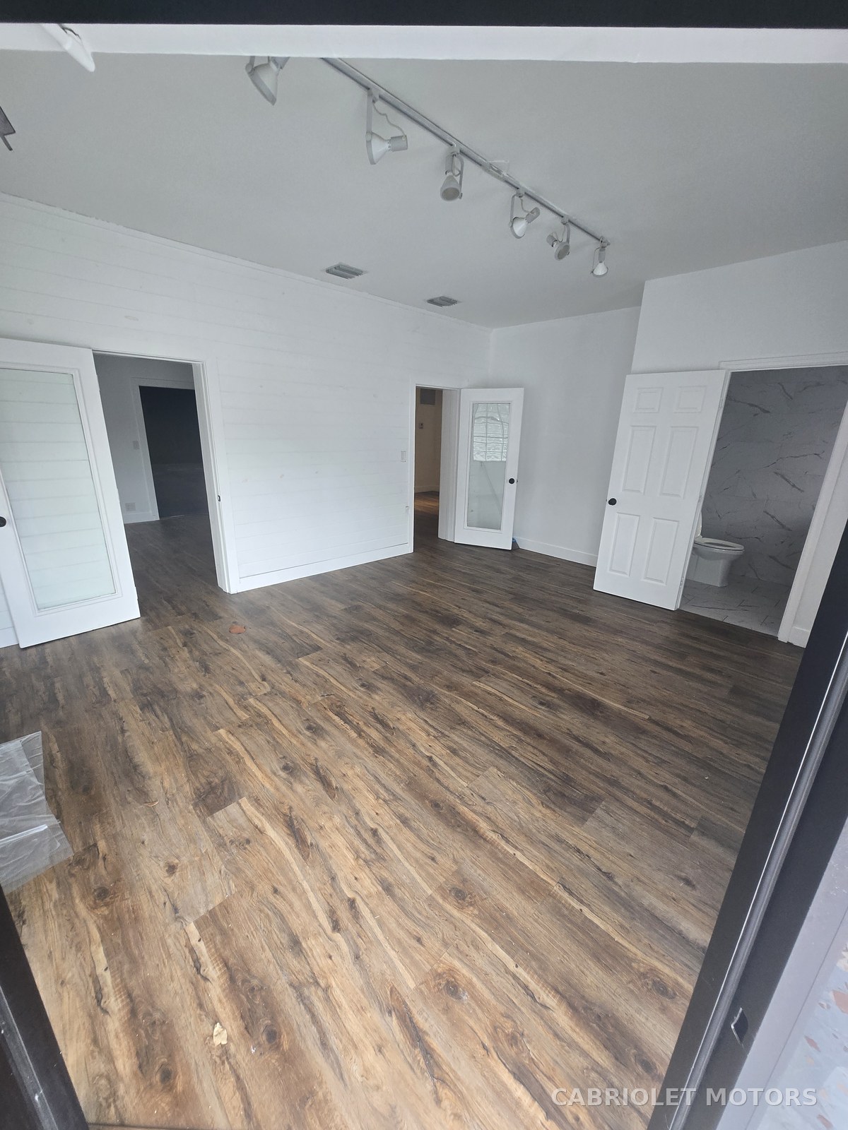 Main customer lobby before renovation, an empty white-walled room with wood-look plank flooring, track lighting and open doorways