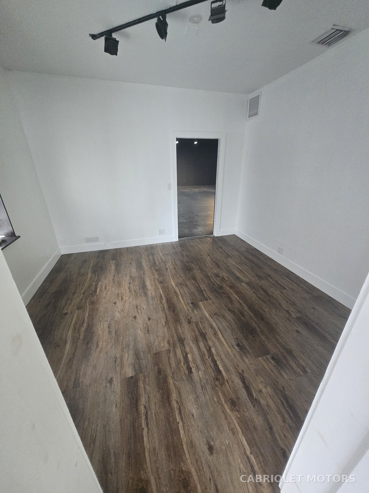 Small secondary office before renovation, an empty white-walled room with wood-look plank flooring and track lighting