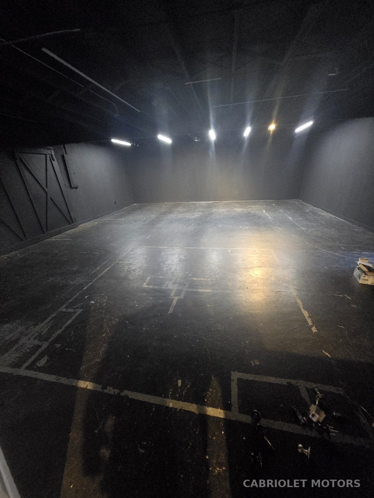 Interior showroom floor before renovation, an empty dark-walled space with bare concrete flooring and existing overhead lighting
